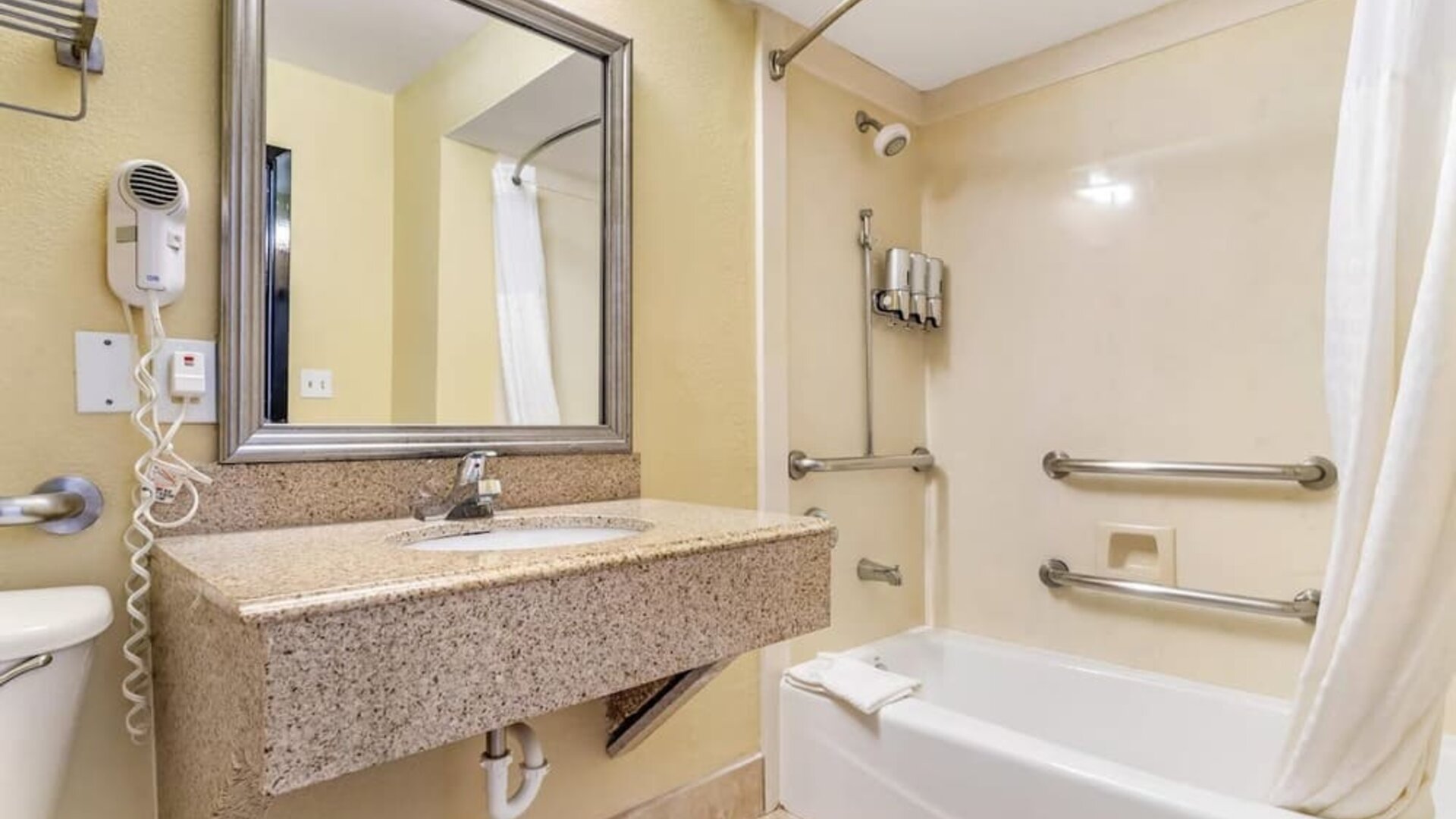 Bathroom with bathtub shower combo, grab bars, sink vanity, and wall-mounted hair dryer at Comfort Suites Bush Intercontinental Airport.