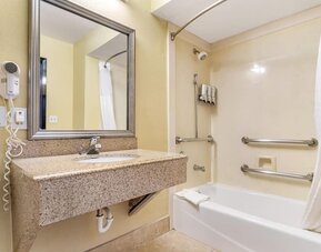Bathroom with bathtub shower combo, grab bars, sink vanity, and wall-mounted hair dryer at Comfort Suites Bush Intercontinental Airport.