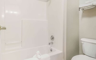 Bathroom with bathtub shower combo, toilet, and folded towels on rack at Suburban Studios Mason Hwy-42.