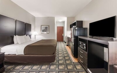 King room with desk area, TV, dresser, and patterned carpet flooring at Suburban Studios Mason Hwy-42.