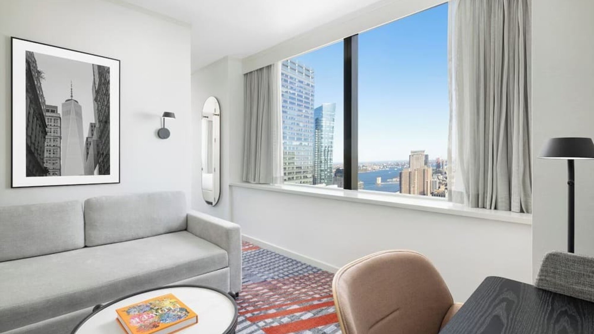 Lounge area with sofa seating, floor lamp, wall art, and large window overlooking city buildings at M Social New York Downtown.