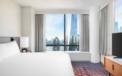 Guest room with king bed, large window, and city skyline view at M Social New York Downtown.