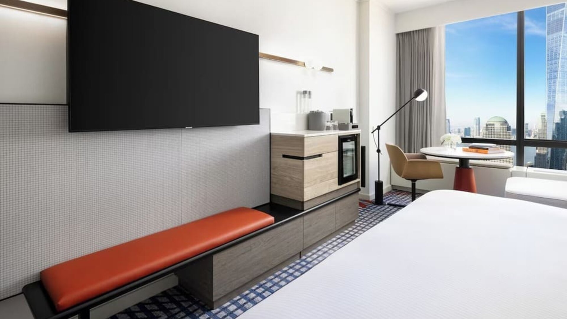 Guest room with wall-mounted TV, minibar, workspace, and modern furnishings at M Social New York Downtown.