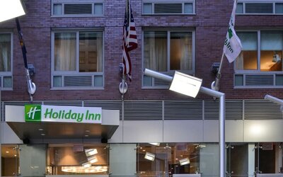 Exterior view of the hotel building façade with signage and flags at Holiday Inn New York City - Times Square By IHG.