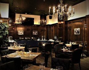 Restaurant dining area with wooden tables, chandeliers, and warm ambient lighting at Holiday Inn New York City - Times Square By IHG.