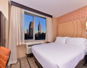 Guest room with king bed and large window showcasing city skyline views at Holiday Inn New York City - Times Square By IHG.