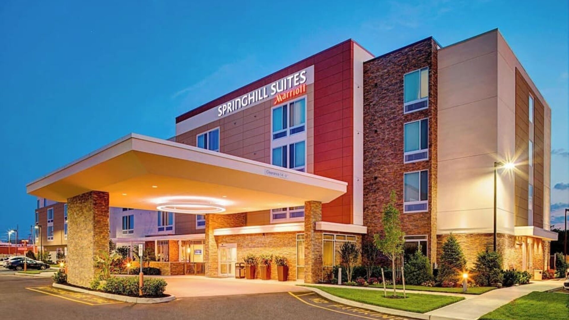 Exterior view of the hotel building with covered entrance and landscaping at Springhill Suites Carle Place.