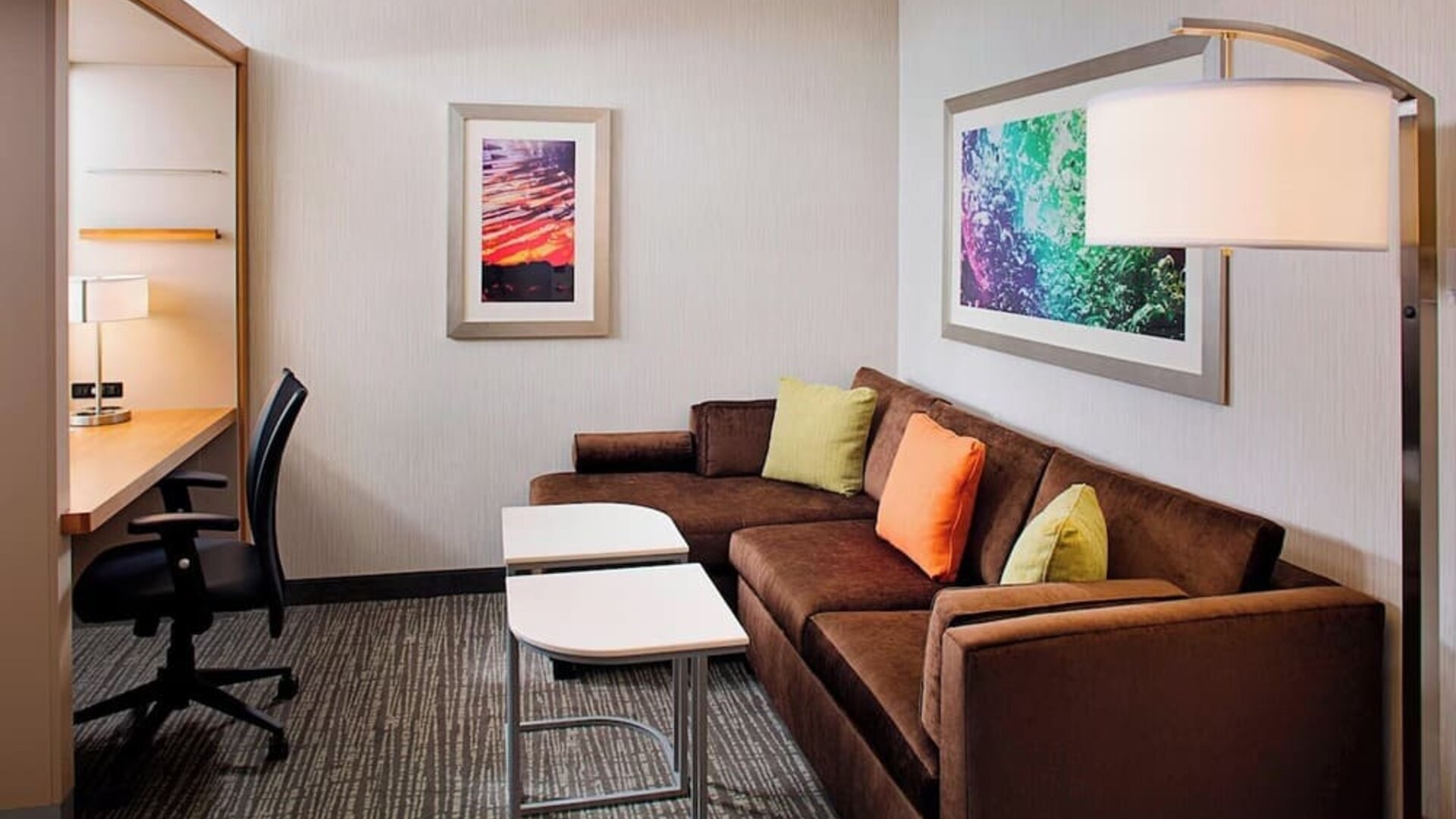 Guest suite with sofa seating area, workspace desk, and modern décor at Springhill Suites Carle Place.