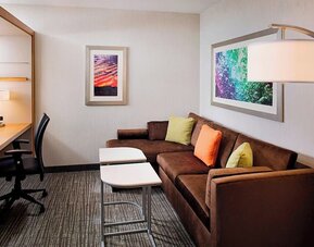 Guest suite with sofa seating area, workspace desk, and modern décor at Springhill Suites Carle Place.