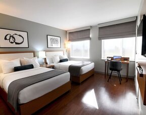 Guest room with two double beds, workspace desk, chair, and large windows at Edge Hotel NYC.