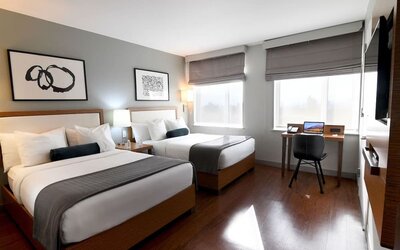 Guest room with two double beds, workspace desk, chair, and large windows at Edge Hotel NYC.