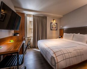 Guest room with king bed, workspace desk, chair, and wall-mounted TV at La Quinta Times Square South.