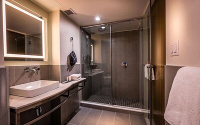 Bathroom with walk-in glass shower, sink, illuminated mirror, and modern finishes at La Quinta Times Square South.