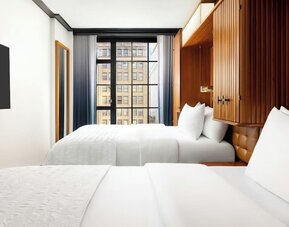 Guest room with two beds, wood-paneled headboard, and large window with city views at Le Méridien New York, Central Park.