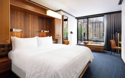 Guest room with king bed, wood accents, and floor-to-ceiling windows with balcony access at Le Méridien New York, Central Park.