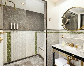 Bathroom with walk-in shower, mosaic tile walls, marble sink, and gold fixtures at Le Méridien New York, Central Park.