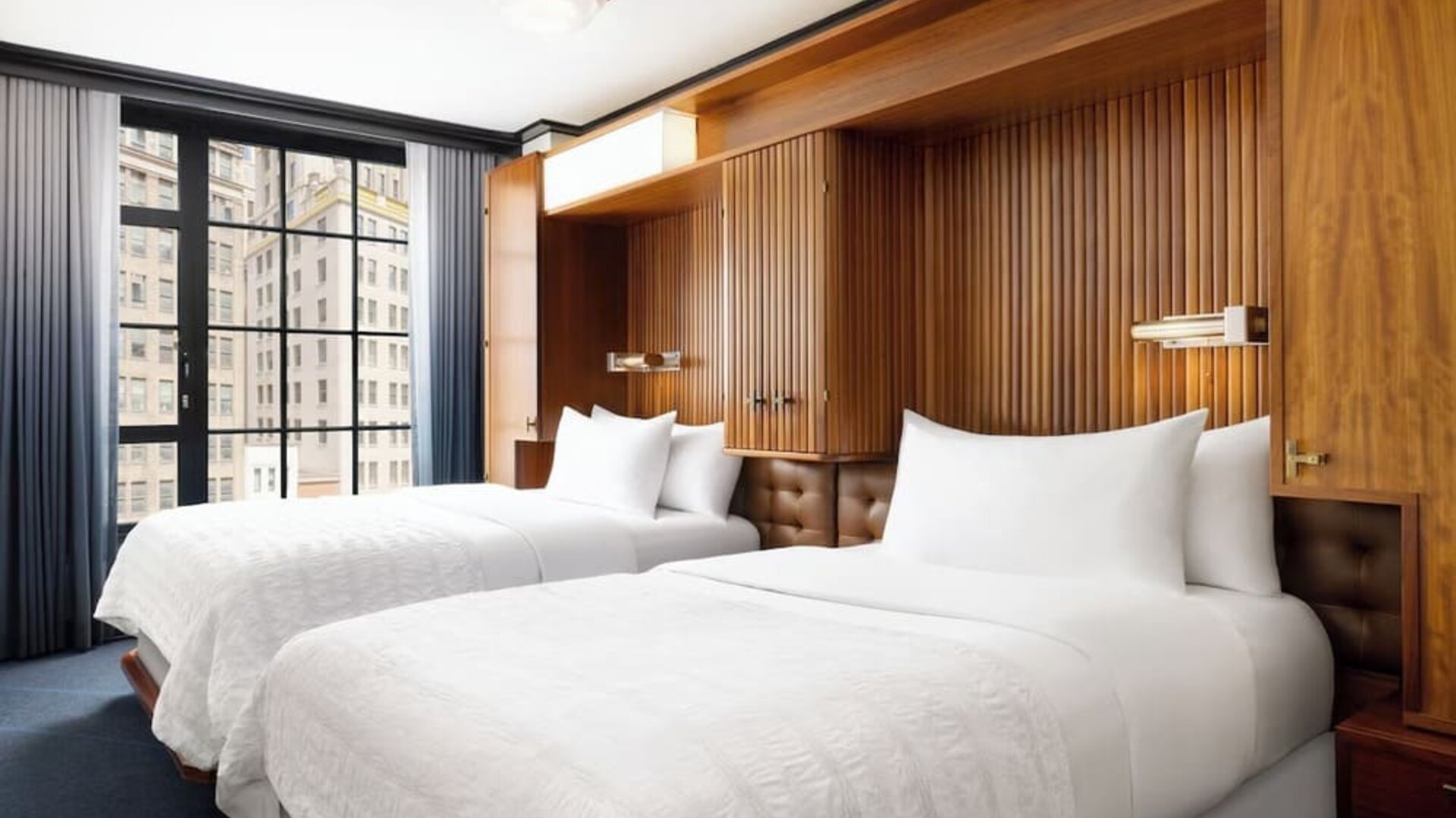 Guest room with two double beds, wood-paneled headboard, and large windows at Le Méridien New York, Central Park.
