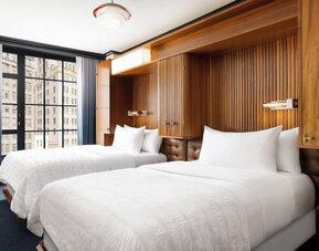 Guest room with two double beds, wood-paneled headboard, and large windows at Le Méridien New York, Central Park.