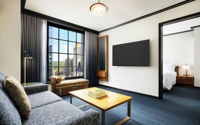 Living area with sofa, coffee table, and connected bedroom space at Le Méridien New York, Central Park.