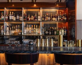 Bar area with shelves of liquor, counter seating, and warm lighting at Le Méridien New York, Central Park.