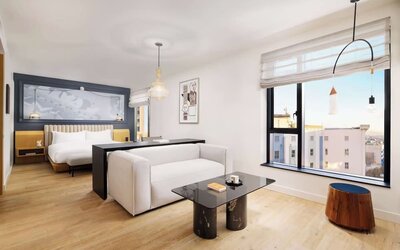 Bright suite with large bed, lounge seating, and expansive city views at Timbri Hotel San Francisco, Curio Collection By Hilton.