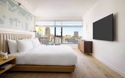 Modern king room with platform bed, wall-mounted TV, wooden furnishings, and large window offering city views at Timbri Hotel San Francisco, Curio Collection By Hilton.