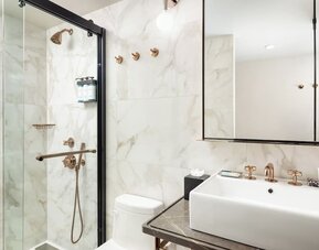 Modern bathroom with walk-in glass shower, marble walls, and sleek vanity with gold fixtures at Hotel Hendricks.