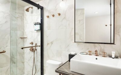 Modern bathroom with walk-in glass shower, marble walls, and sleek vanity with gold fixtures at Hotel Hendricks.