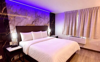 Modern guest room with king bed, marble feature wall, ambient LED lighting, and window with curtains at Imperial Hotel.