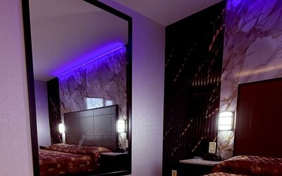Guest room with large wall mirror, bed with patterned bedding, and accent lighting creating a cozy atmosphere at Imperial Hotel.