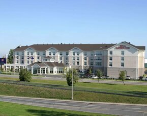 Hotel exterior with green garden at Hilton Garden Inn Montreal Airport.