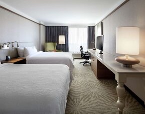 Day use room with two beds, table, lampshade, and work desk at Hilton Garden Inn Montreal Airport.