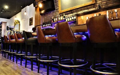 Bar area with high stools, wooden finishes, and illuminated shelving at Holiday Inn New York City - Times Square By IHG.