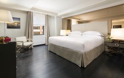 Bright guest room with large windows, neutral tones, and cozy seating at The Michelangelo New York.