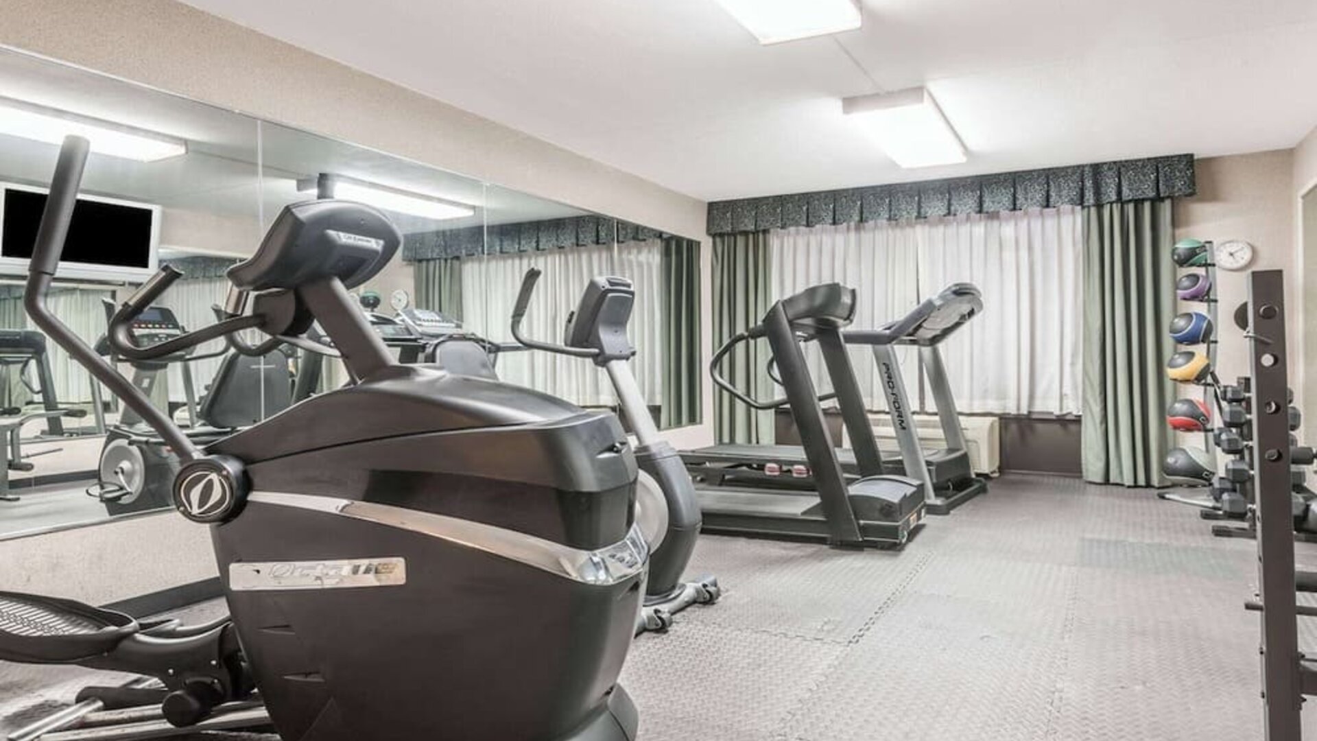 Fitness center with cardio machines, free weights, and mirrored wall at Wyndham Garden Williamsburg Busch Gardens Area.