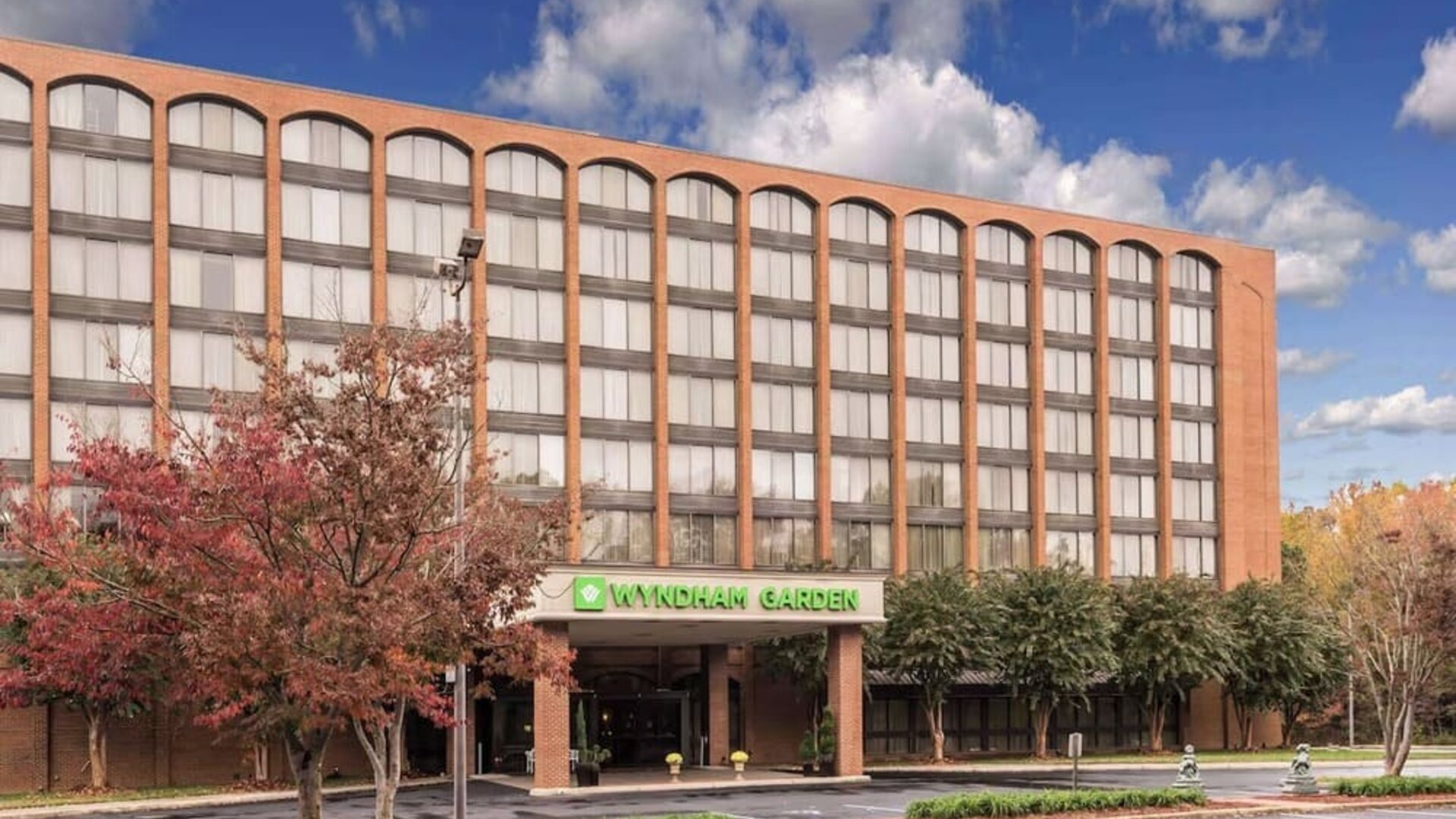 Hotel exterior with Wyndham Garden signage, covered entrance, and parking area at Wyndham Garden Williamsburg Busch Gardens Area.