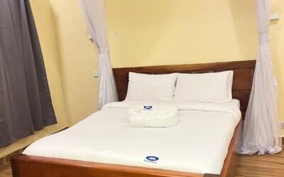 Cozy bedroom at Sega Lodge featuring a wooden bed with white linens, soft canopy drapes, and warm-toned walls.