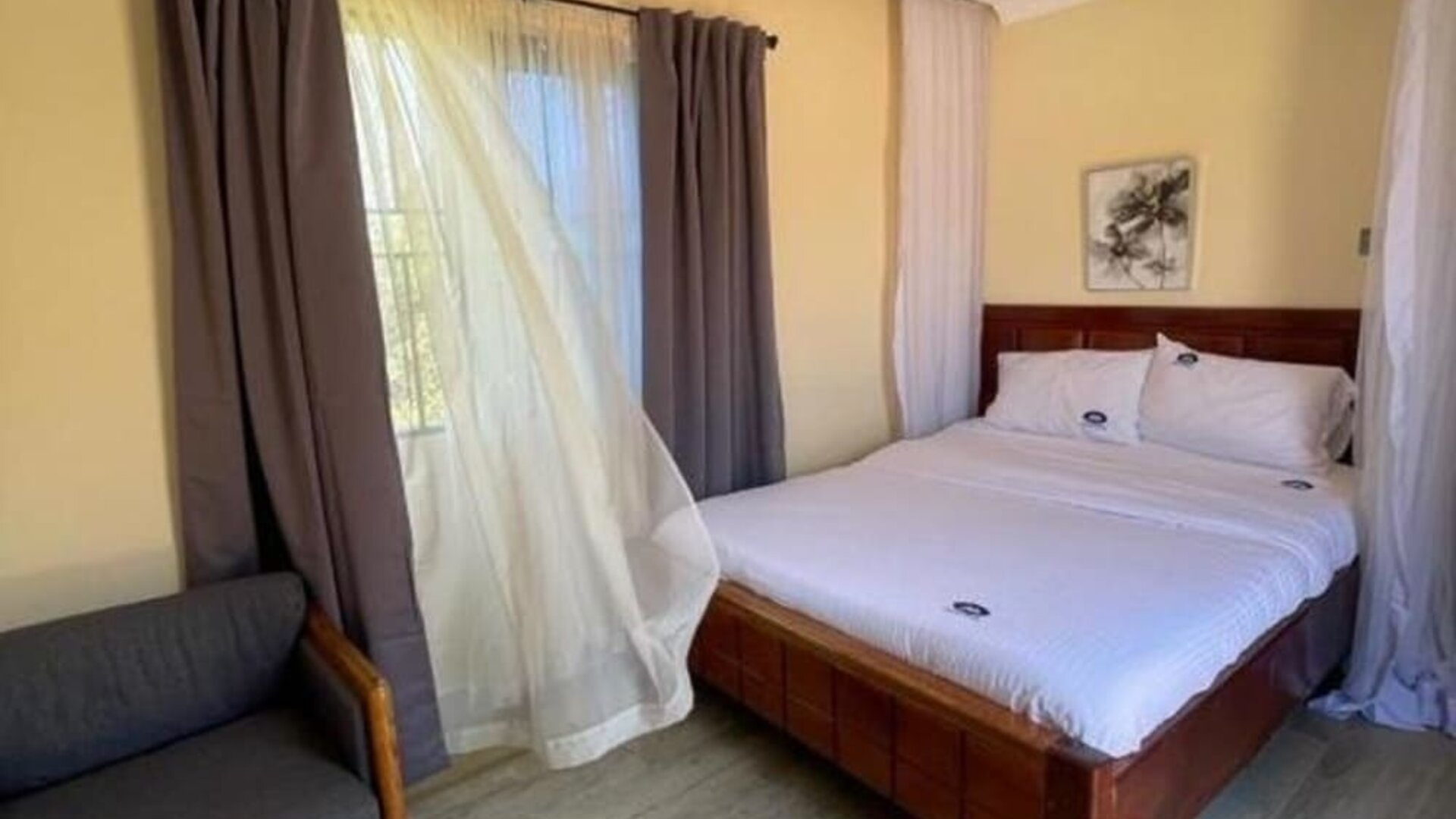 Bright guest room with a canopy-style bed, large window with sheer and blackout curtains, and a comfortable seating area at Sega Lodge.