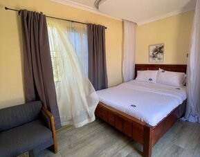 Bright guest room with a canopy-style bed, large window with sheer and blackout curtains, and a comfortable seating area at Sega Lodge.