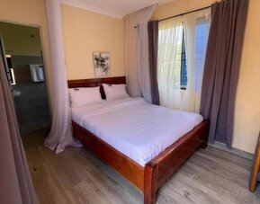 Spacious bedroom with a wooden double bed, canopy frame, and natural light streaming through curtained windows at Sega Lodge.