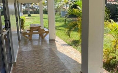 Covered patio area with tiled flooring and picnic-style seating, overlooking the garden at Sega Lodge.
