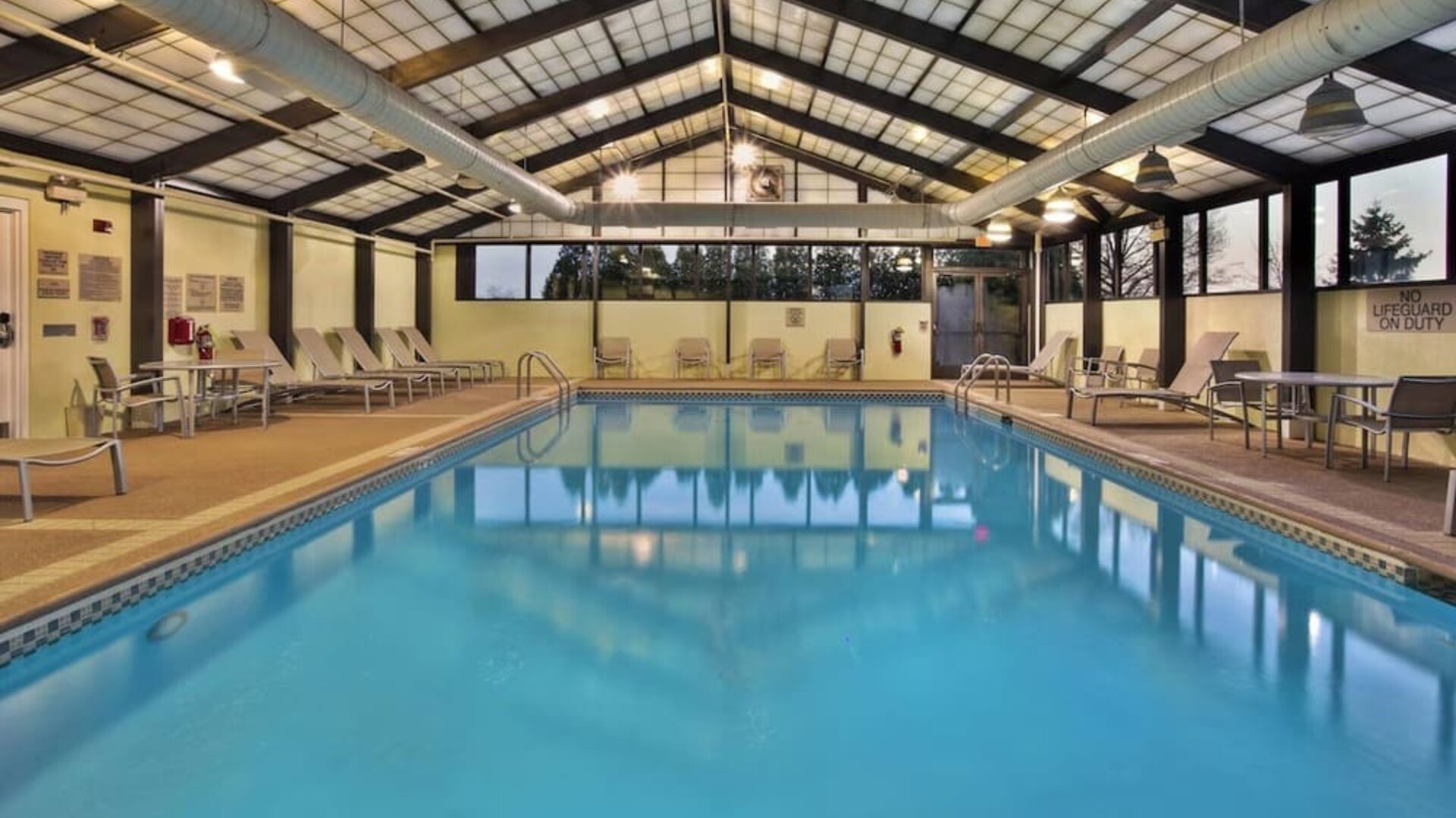 Indoor pool with lounge chairs, skylit ceiling, and large windows along the deck at Marriott SpringHill Suites Naperville/Warrenville.