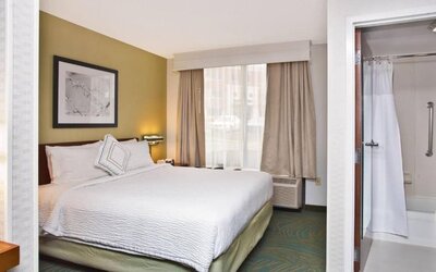 Guest room with king bed, white bedding, window with curtains and an armchair at Marriott SpringHill Suites Naperville/Warrenville.
