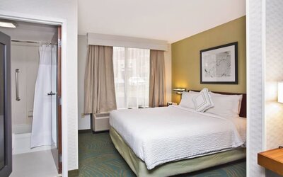 King guest room with white bedding, work desk, window seating area, and accessible bathroom at Marriott SpringHill Suites Naperville/Warrenville.
