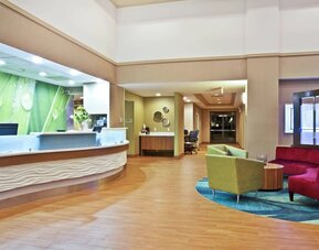 Lobby with curved front desk, green accent wall, wood flooring, and colorful lounge seating area at Marriott SpringHill Suites Naperville/Warrenville.