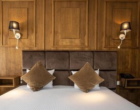 Double bed with padded headboard, wood-paneled wall, and wall-mounted lamps creating a warm, cozy setting at Hôtel Espérance.