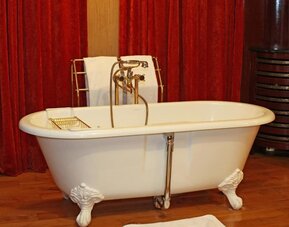Close-up of vintage clawfoot tub with handheld shower, brass taps, and red curtain backdrop at Hôtel Espérance.