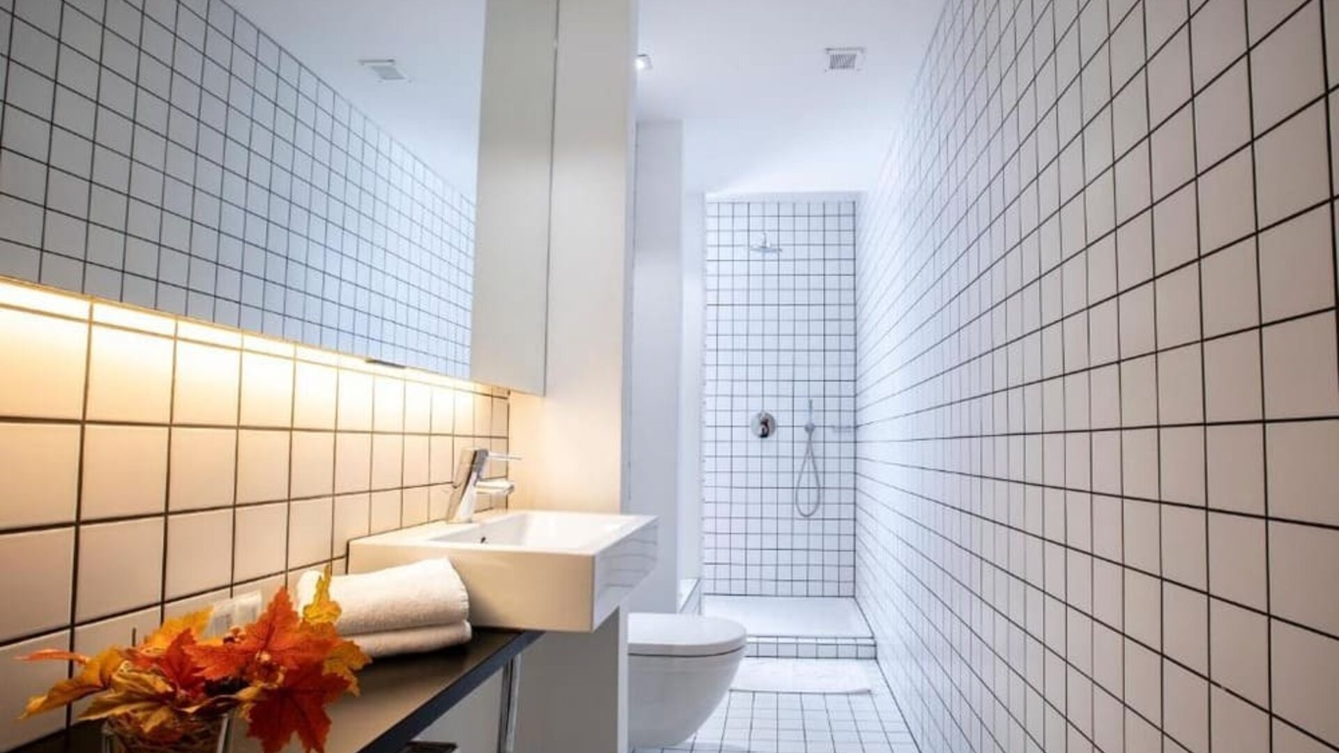 Modern tiled bathroom with wall-mounted sink, toilet, walk-in shower, and minimalist lighting at Hôtel Espérance.
