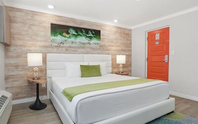 Queen bedroom with upholstered headboard, bedside lamps, artwork, and bright orange entry door at Chesterfield Hotel & Suites.