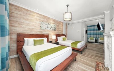 Guest room with two beds, wood headboards, green runners, seating area, and wall-mounted TV at Chesterfield Hotel & Suites.